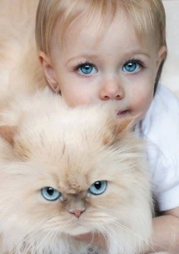A baby and a cat are looking at the camera.